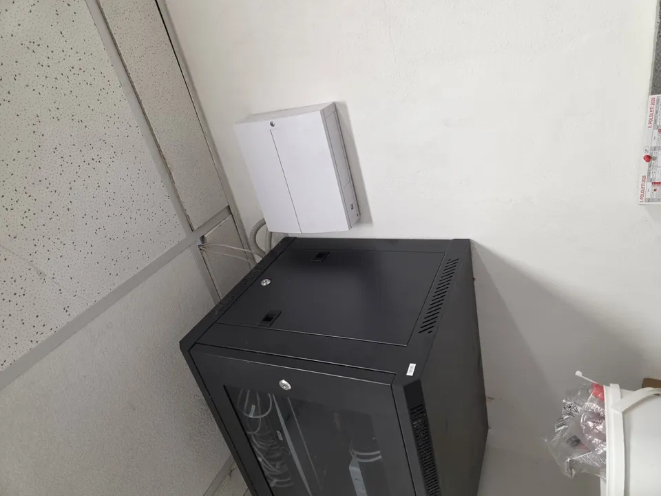 Černý nástěnný rack a bílá skříň zabezpečovacího systému pod stropním podhledem.
