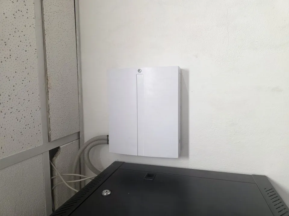 Bílá skříň zabezpečení u černého racku s kabely vedenými v chráničkách od stropu.