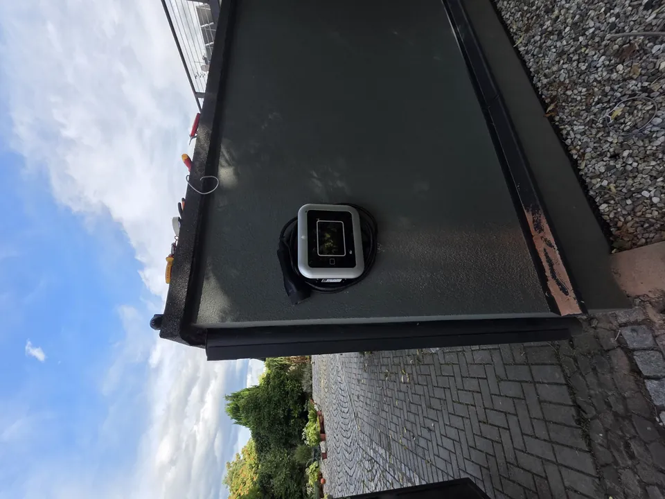 Venkovní nástěnný wallbox se svinutým černým nabíjecím kabelem u brány do dvora.